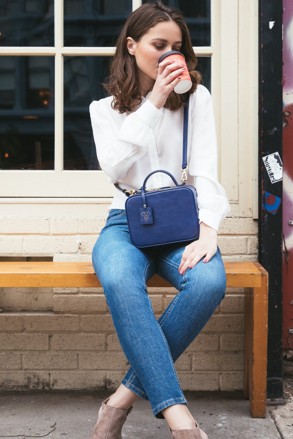 Model wearing FERRON crossbody vegan handbag and drinking coffee
