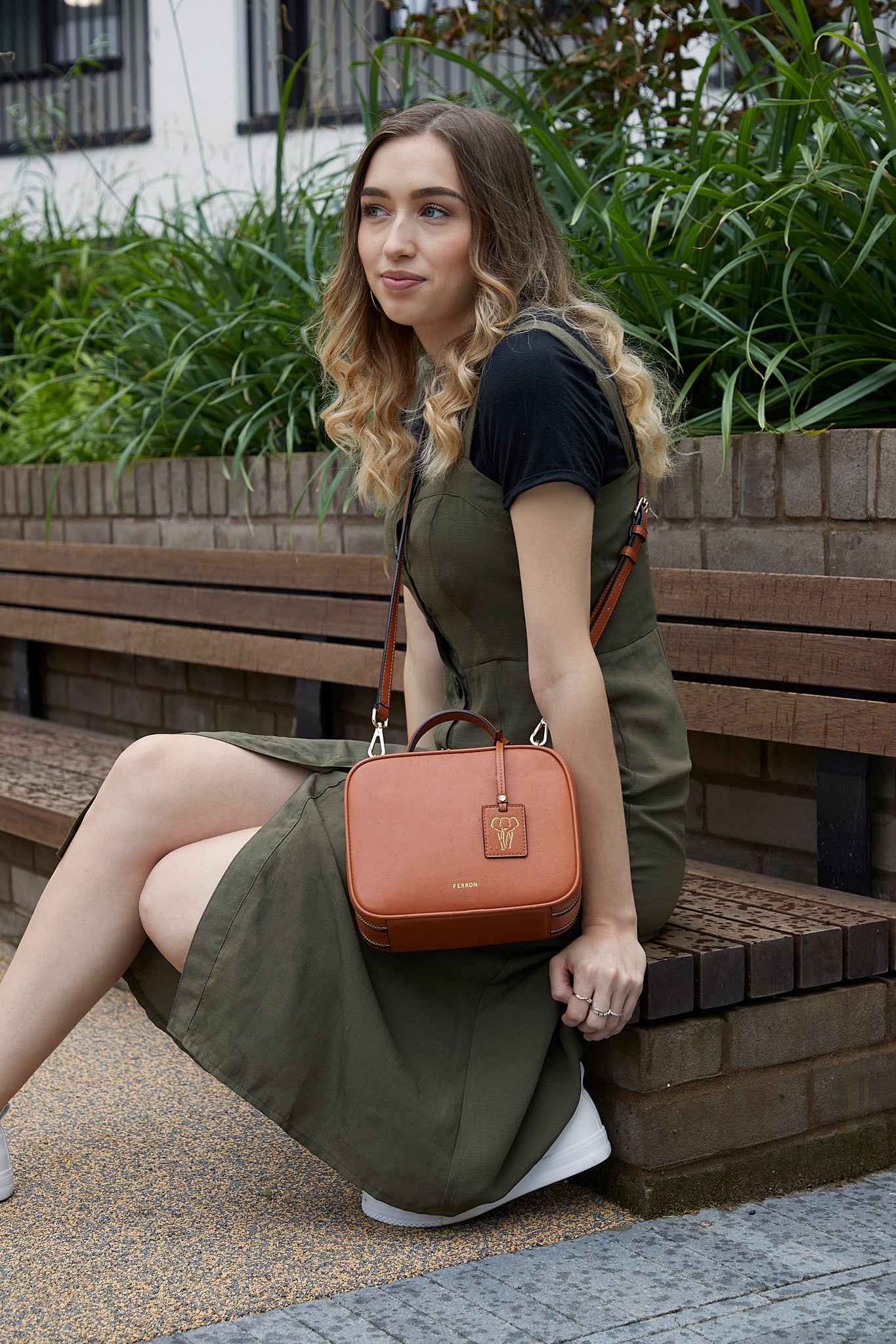 Model sitting wearing FERRON Vegan Signature Crossbody bag in tan with adjustable and detachable straps